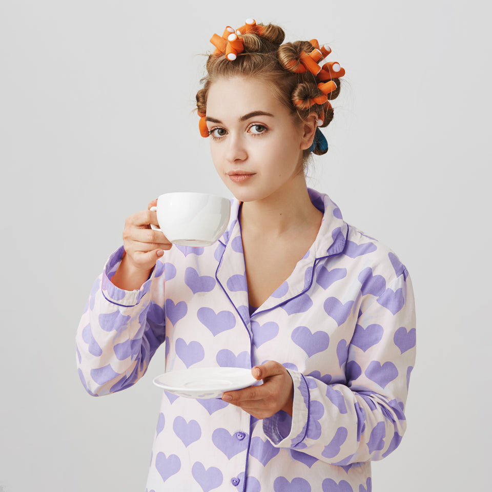 Lullaby tea ticket to snoozeland. Girl with orange curlers in hair, clutching a cup of tea wearing cute pyjamas with purple heart fabric. 
