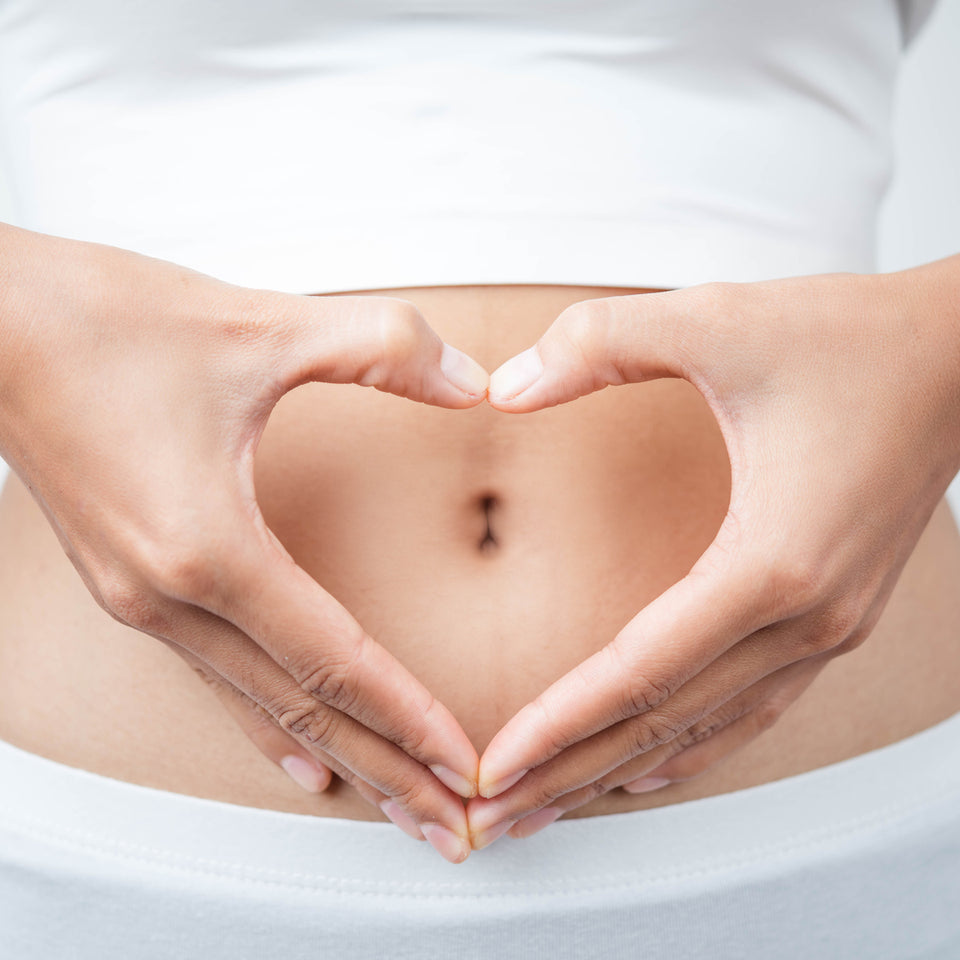 Flat tummy picture. Woman's tummy with bare midriff and white crop and tights, hands creating a heart shape around the navel to represent a happy tummy. Digestive health. Digestive teas.