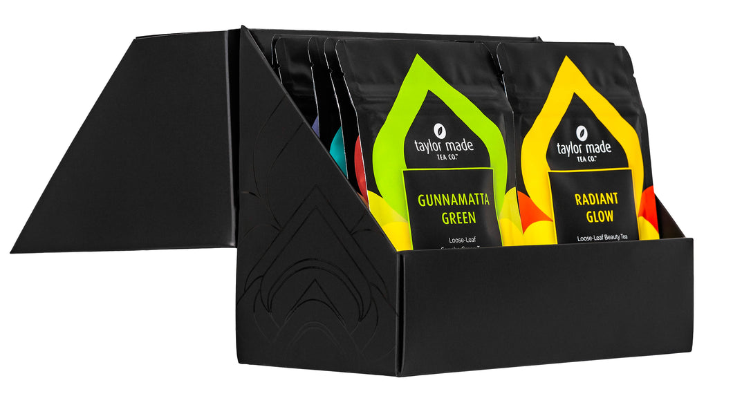 Discovery Box with luxury organic loose leaf teas and collagen peptides. Satin finish black box with 9 pouches of loose leaf tea and 1 pouch of collagen peptides powder. Gift Pack. Loose leaf tea gift pack. Open side view., 10 pouches standing in 2 rows of 5. Gunnamatta Green and Radiant Glow at the front
